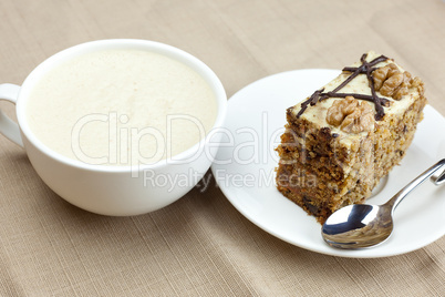 A cup of cappuccino, a piece of cake with nuts and spoon lying o