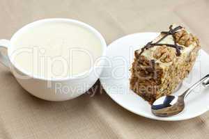 A cup of cappuccino, a piece of cake with nuts and spoon lying o