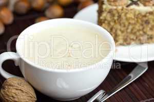 cup of cappuccino, a piece of cake with nuts on a plate lying on