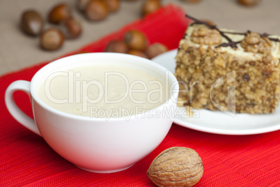 cup of cappuccino, a piece of cake with nuts on a plate lying on