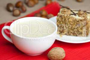 cup of cappuccino, a piece of cake with nuts on a plate lying on