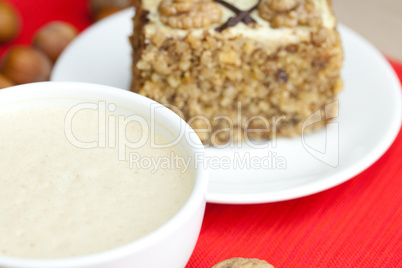 cup of cappuccino, a piece of cake with nuts on a plate lying on