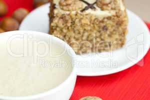 cup of cappuccino, a piece of cake with nuts on a plate lying on