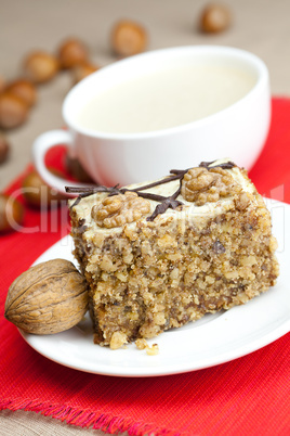 cup of cappuccino, a piece of cake with nuts on a plate lying on