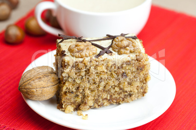 cup of cappuccino, a piece of cake with nuts on a plate lying on