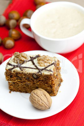 cup of cappuccino, a piece of cake with nuts on a plate lying on