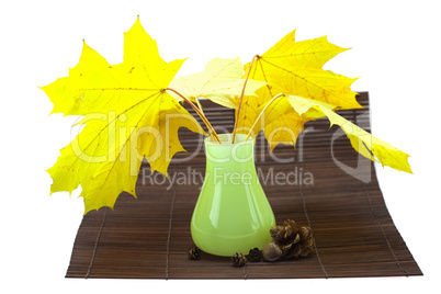 yellow maple leaves and buds in a vase on a bamboo mat