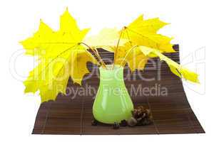yellow maple leaves and buds in a vase on a bamboo mat