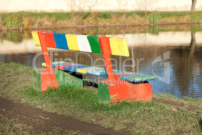 multi-colored bench standing in a park near the pond