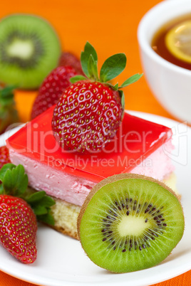 lemon tea, kiwi,cake and strawberries lying on the orange fabric