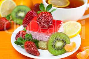 lemon tea, kiwi,cake and strawberries lying on the orange fabric