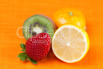 kiwi,lemon,mandarin and strawberries lying on the orange fabric
