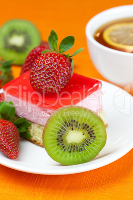 lemon tea, kiwi,cake and strawberries lying on the orange fabric