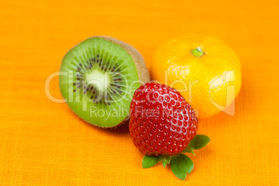 kiwi,mandarin and strawberries lying on the orange fabric