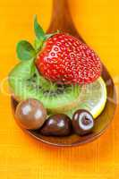 Strawberries, kiwi and chocolate candy in the wooden spoon of th