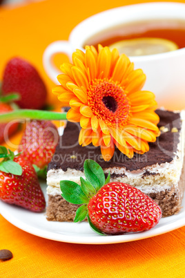 gerbera, lemon tea, cake and strawberries lying on the orange fa