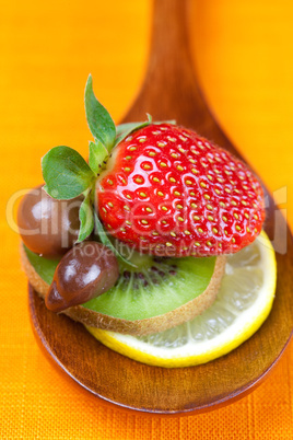 Strawberries, kiwi and chocolate candy in the wooden spoon of th