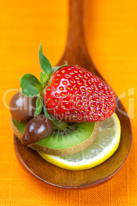 Strawberries, kiwi and chocolate candy in the wooden spoon of th