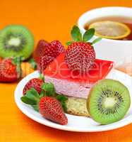 lemon tea, kiwi,cake and strawberries lying on the orange fabric