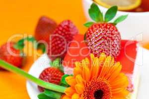 gerbera, lemon tea, cake and strawberries lying on the orange fa