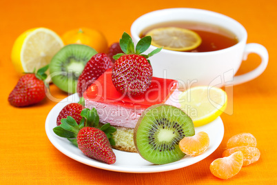 lemon tea, kiwi,cake and strawberries lying on the orange fabric