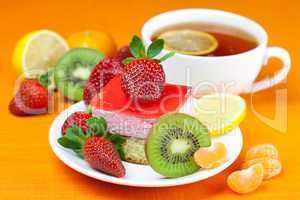 lemon tea, kiwi,cake and strawberries lying on the orange fabric