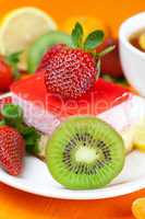 lemon tea, kiwi,cake and strawberries lying on the orange fabric