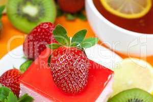 lemon tea, kiwi,cake and strawberries lying on the orange fabric