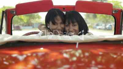 Beautiful twin sisters hugging in vintage convertible car
