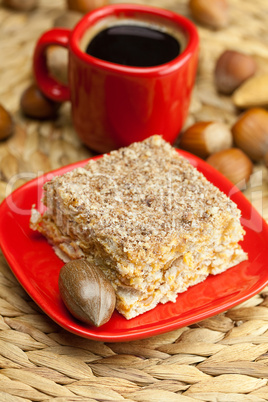 cake on a plate, nuts and a cup of coffee on a wicker mat