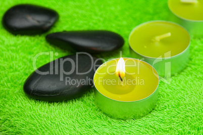 burning candle and spa black stones lying on the towel