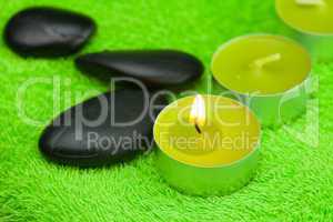 burning candle and spa black stones lying on the towel