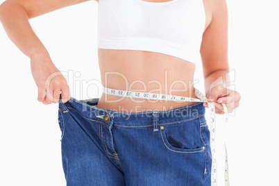 Woman measuring her waist while wearing too big jeans