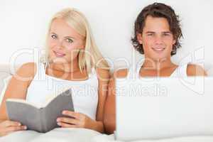 Man with a laptop while his girlfriend is reading a book