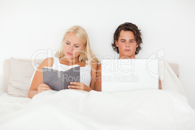 Man using a laptop while his girlfriend is reading a book