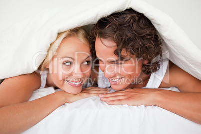 Couple under a duvet with a knowing smile