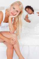 Portrait of an unhappy woman sitting on a bed while her fiance i