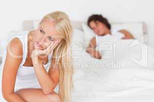 Upset woman sitting on a bed while her fiance is sleeping