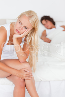 Portrait of an upset woman sitting on a bed while her fiance is