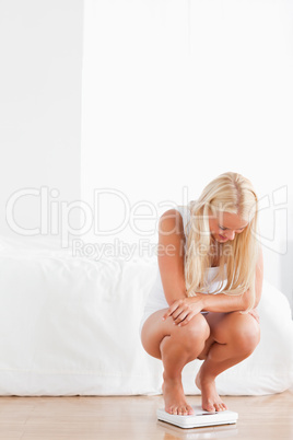 Portrait of a blonde woman squatting on a weighing machine