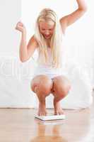 Portrait of a cheerful woman squatting on a weighing machine