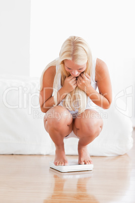 Portrait of a cute woman squatting on a weighing machine