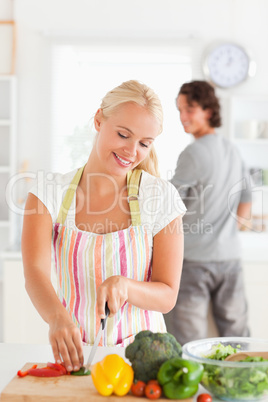 Portrait of a woman slicing pepper while her boyfriend is lookin