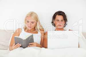 Woman reading a book while her boyfriend is using a laptop
