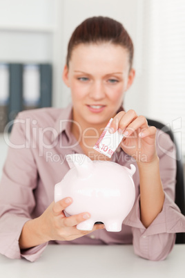A businesswoman inserting money in piggy bank