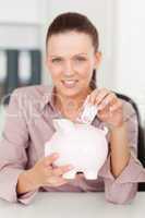 Businesswoman putting money into piggy bank