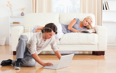 Man using a laptop while his girlfriend is reading a book