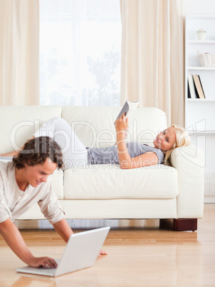 Portrait of a man using a laptop while his wife is reading a boo