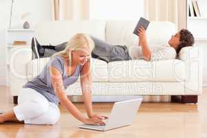 Portrait of a woman using a laptop while her boyfriend is readin