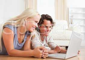 Couple using a laptop while lying on the floor